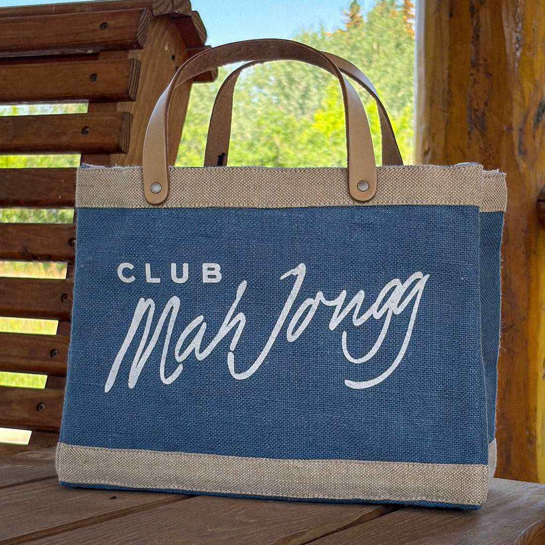 A blue and beige jute tote bag with tan leather handles, featuring the text &