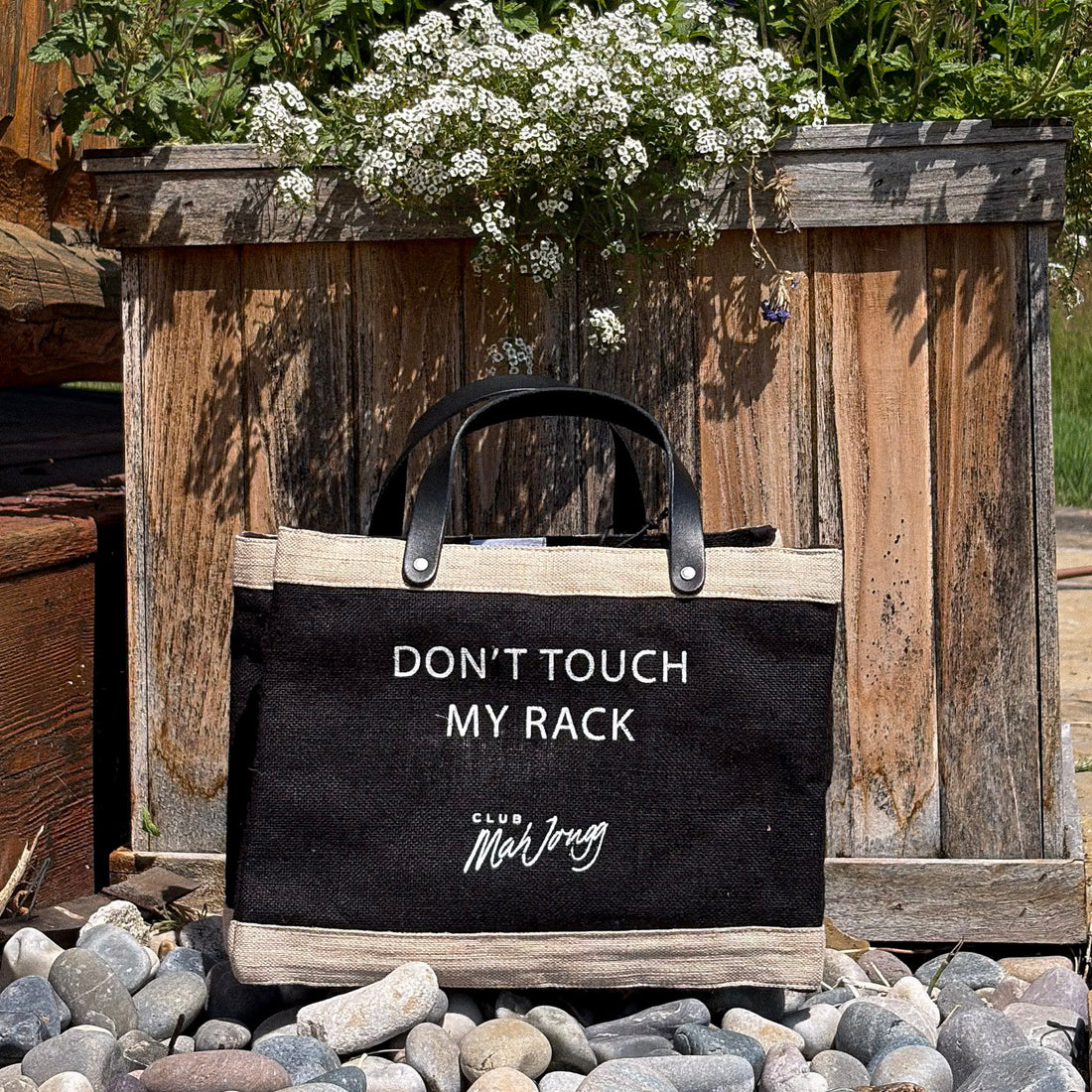 A black jute tote bag with black leather handles with text &