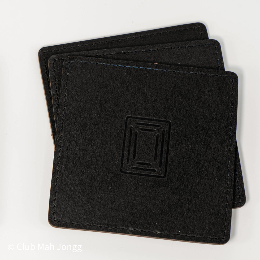 Stack of black square leather mahjong coasters with embossed Club Mah Jongg icon