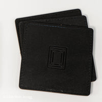 Stack of black square leather mahjong coasters with embossed Club Mah Jongg icon